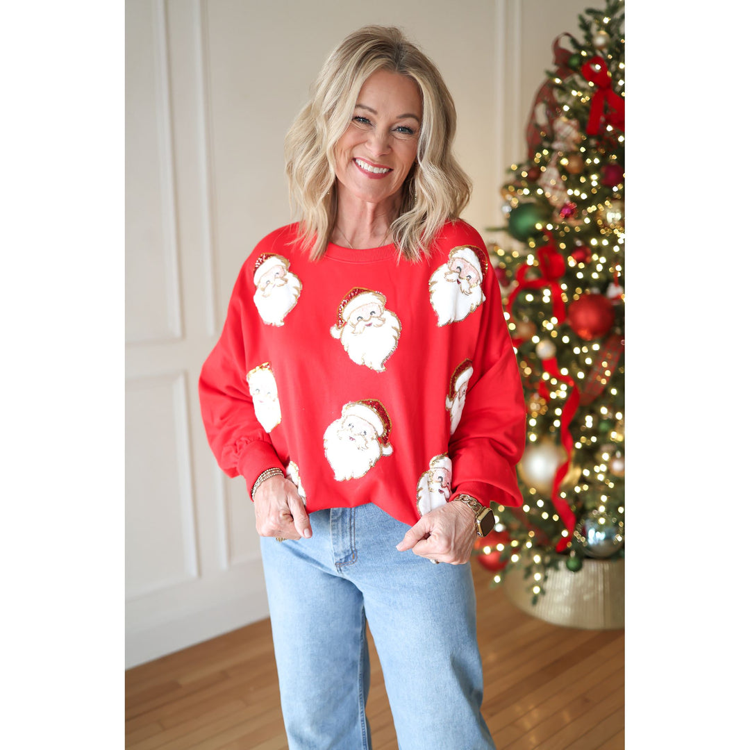 Woman wearing a red sweater with white Santa Claus prints in front of a decorated Christmas tree.