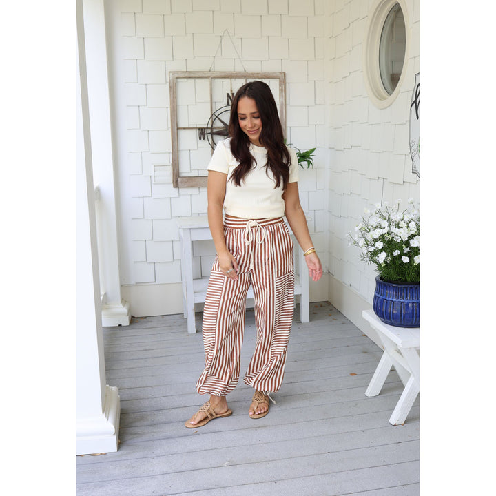 Woman in white top and striped pants standing on a wooden deck with white walls and decorative elements.