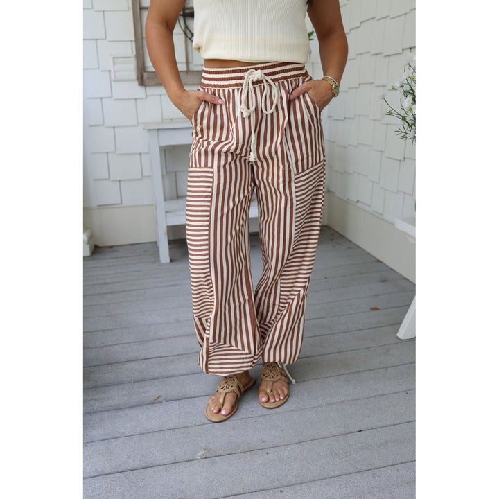 Person wearing brown and white striped pants on a wooden deck.
