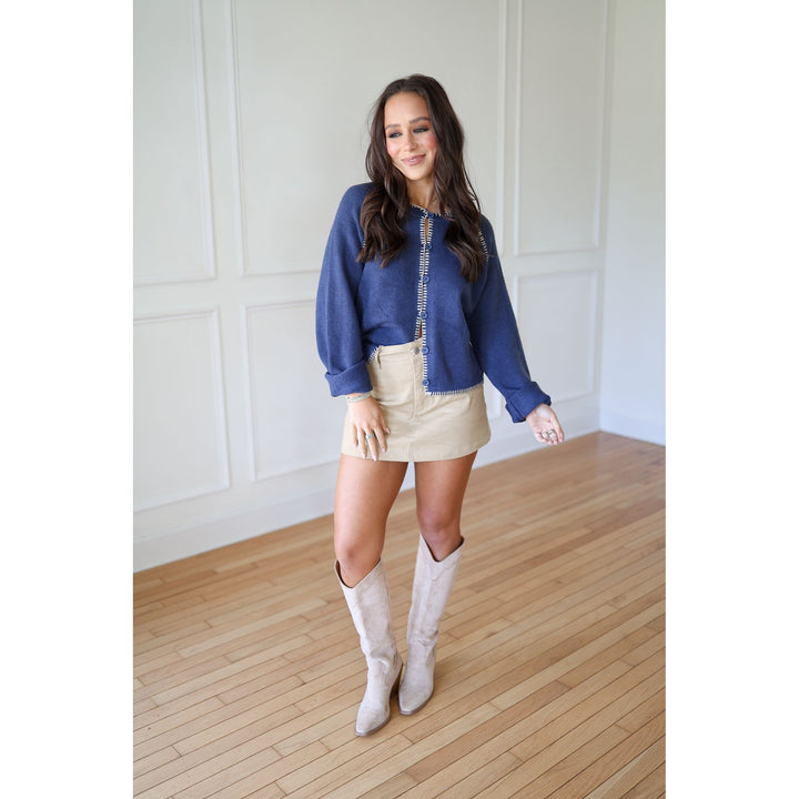 Woman wearing a blue sweater, beige skirt, and white boots 