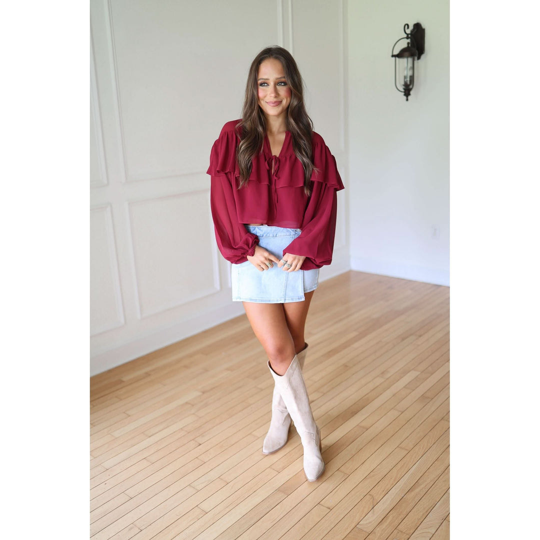 Woman wearing a burgundy blouse, light blue skirt, and white knee-high boots