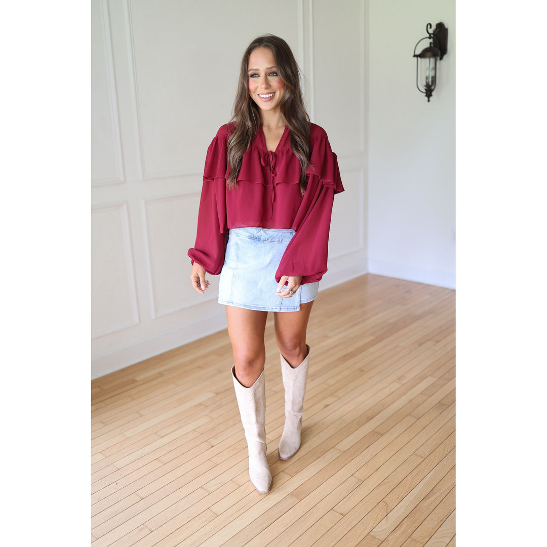 Woman wearing a burgundy blouse, light blue denim skirt, and white knee-high boots 
