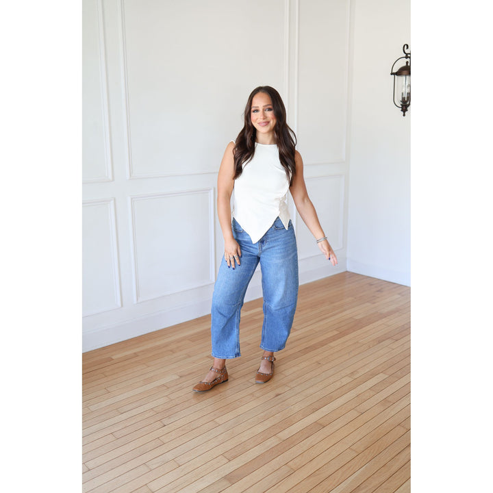 Woman in a white top and blue jeans standing in a room with wooden flooring and white walls.