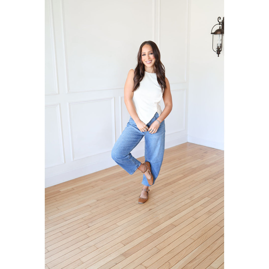 Woman in a white top and blue jeans standing in a room with wooden flooring and white walls.