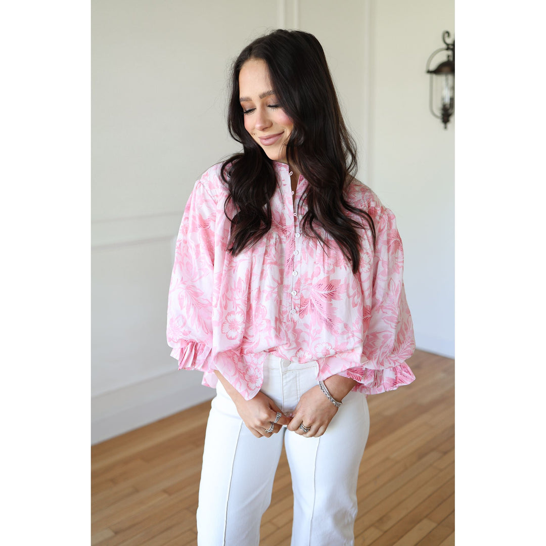 Woman wearing a pink tie-dye blouse and white pants indoors.