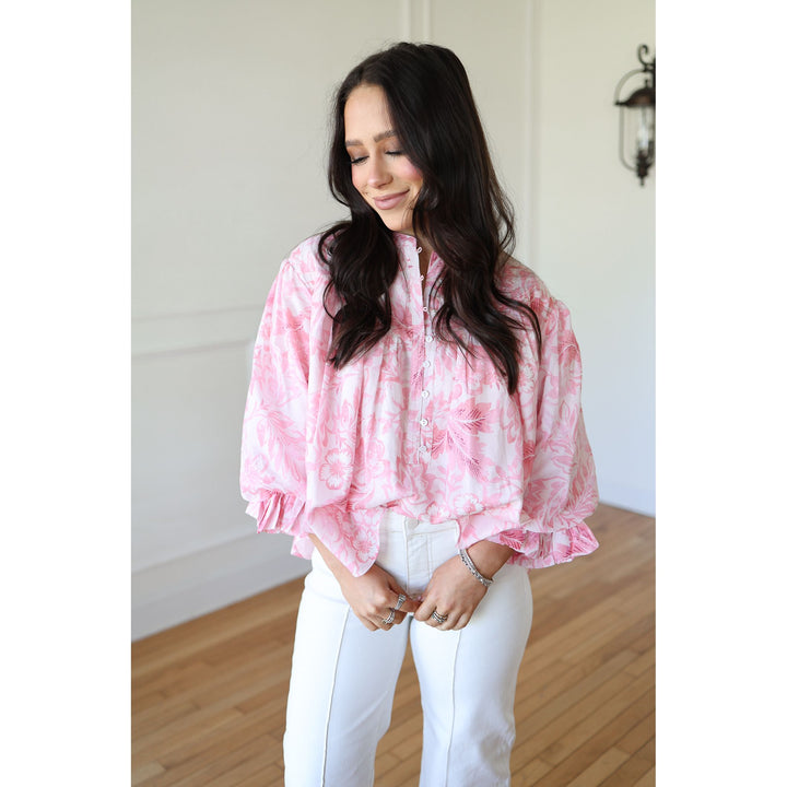 Woman wearing a pink tie-dye blouse and white pants indoors.