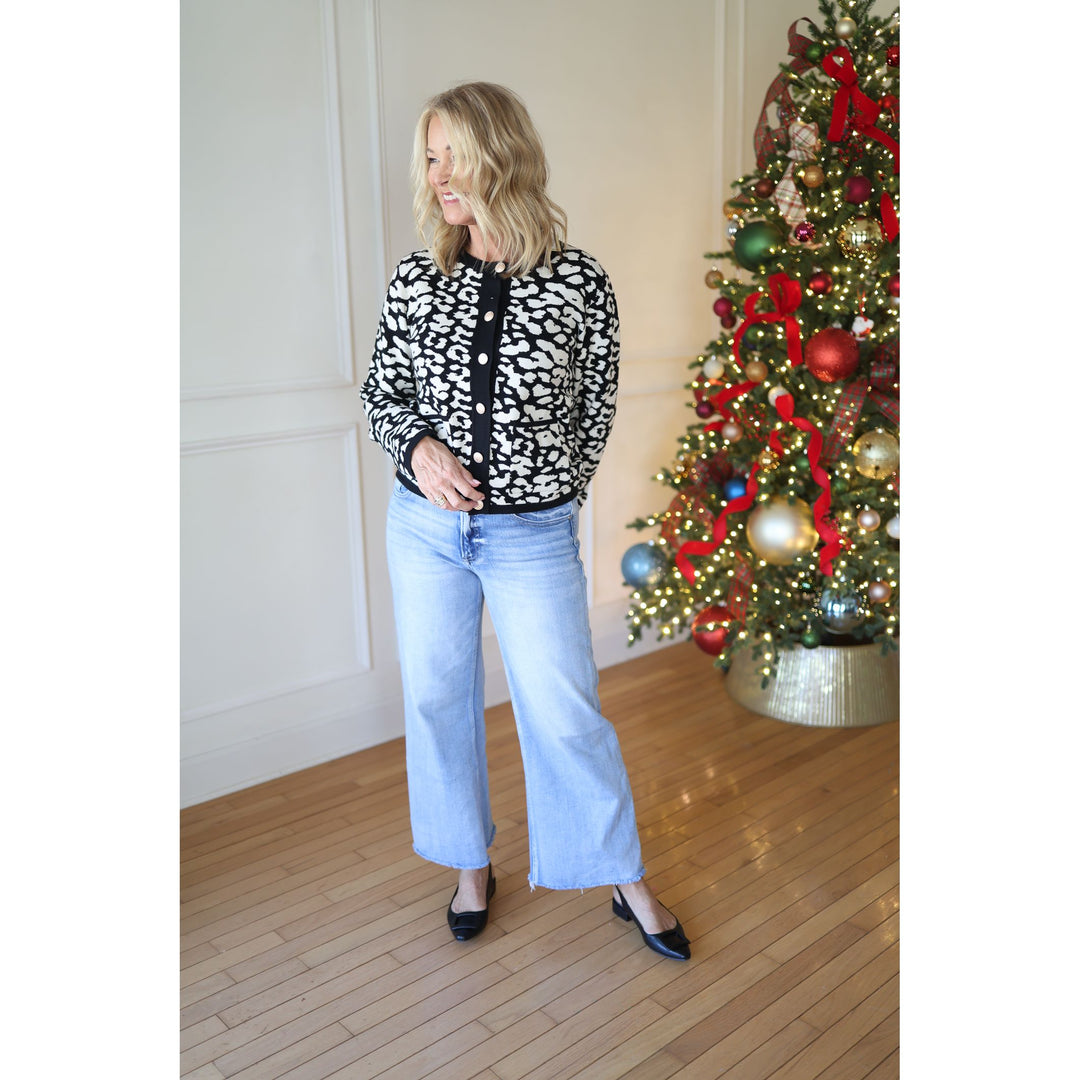 Woman in a leopard print cardigan and jeans standing next to a decorated Christmas tree.