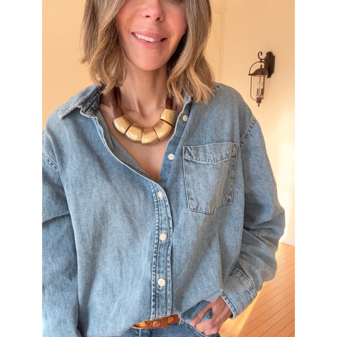 Woman wearing a denim shirt and gold necklace indoors.