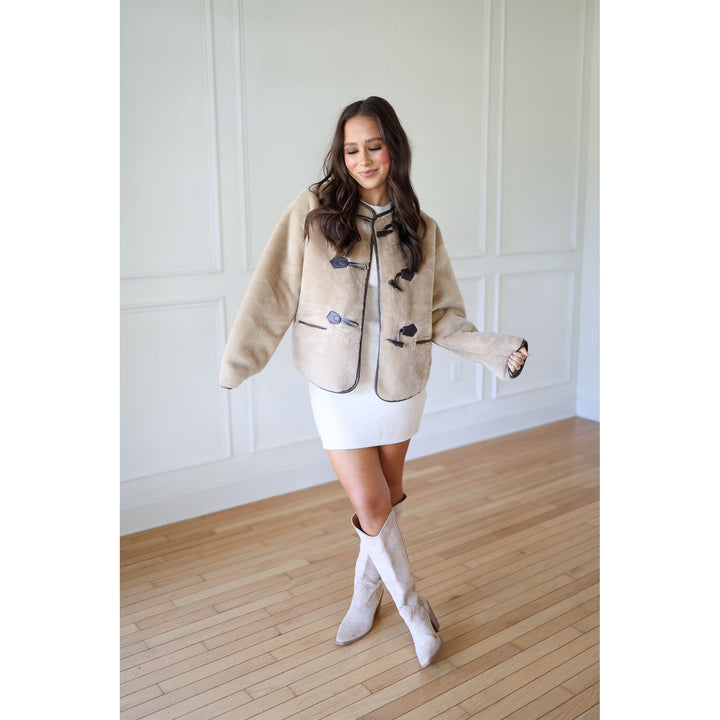 Woman wearing a beige jacket with blue buttons, white skirt, and white knee-high boots 