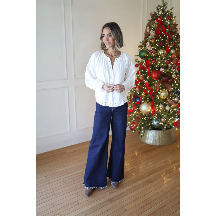 Woman in a white blouse and blue jeans standing in front of a decorated Christmas tree.