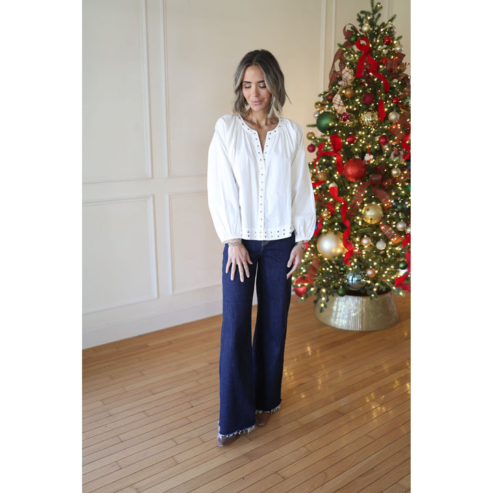 Woman in a white blouse and blue pants standing in front of a decorated Christmas tree.