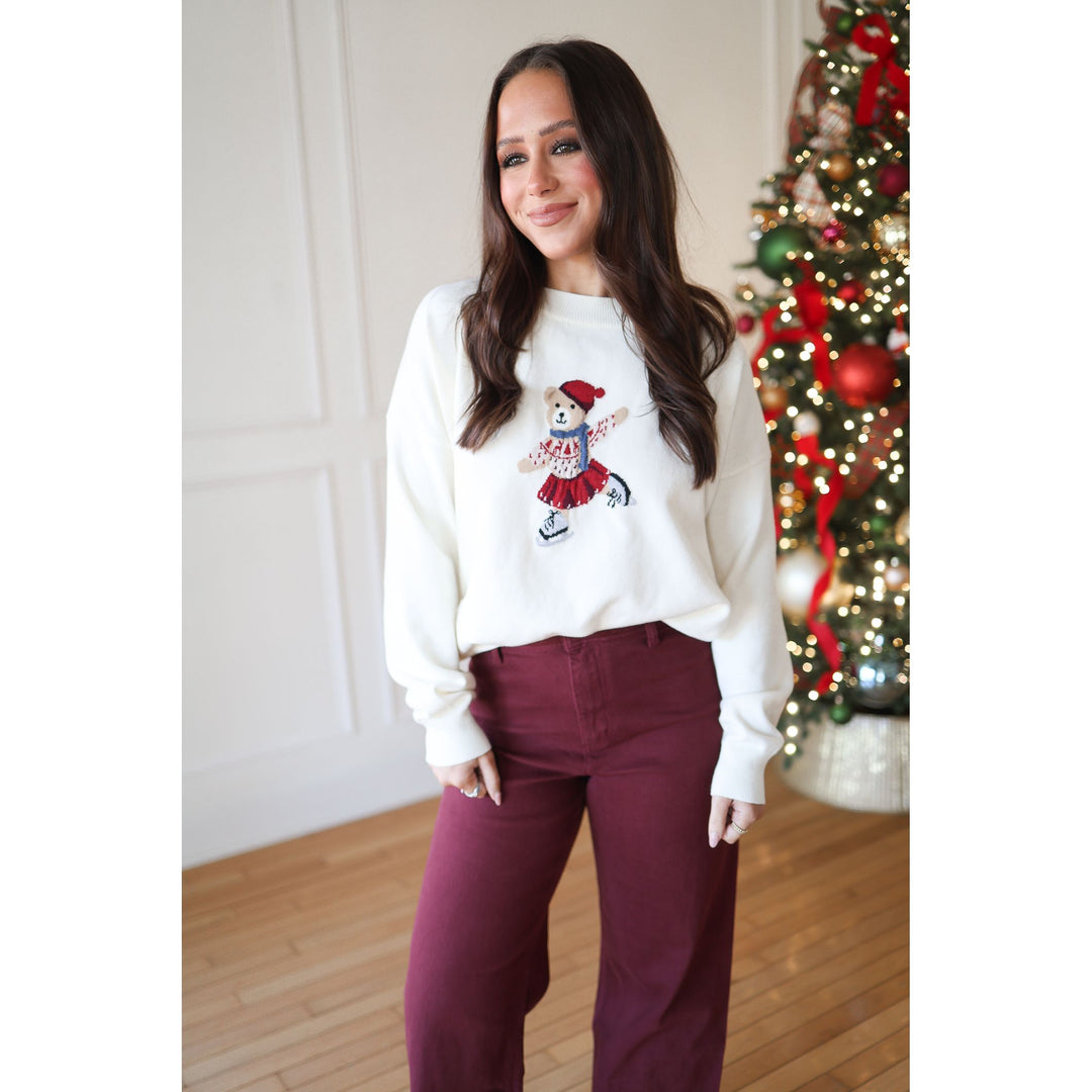 Woman wearing a white sweatshirt with a graphic design in a room with a decorated Christmas tree.