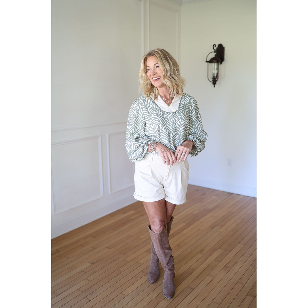 Woman wearing a patterned blouse, white shorts, and brown knee-high boots 