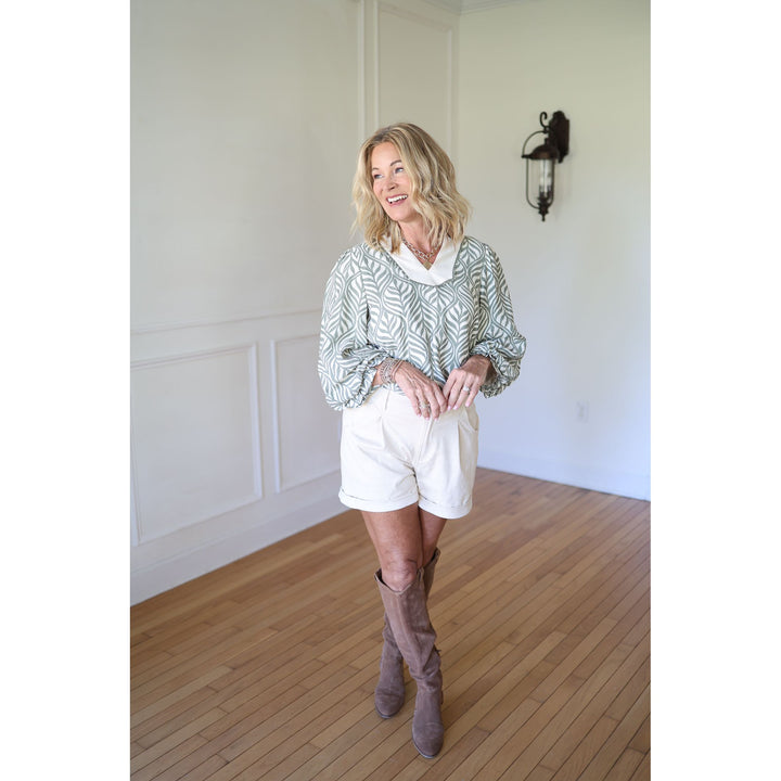 Woman wearing a patterned blouse, white shorts, and brown knee-high boots 