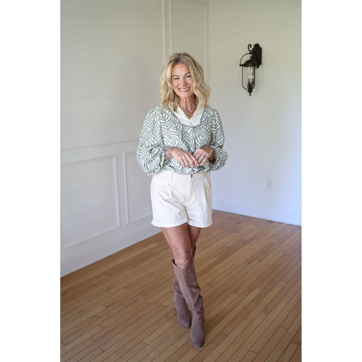 Woman wearing a patterned blouse, white shorts, and brown knee-high boots 
