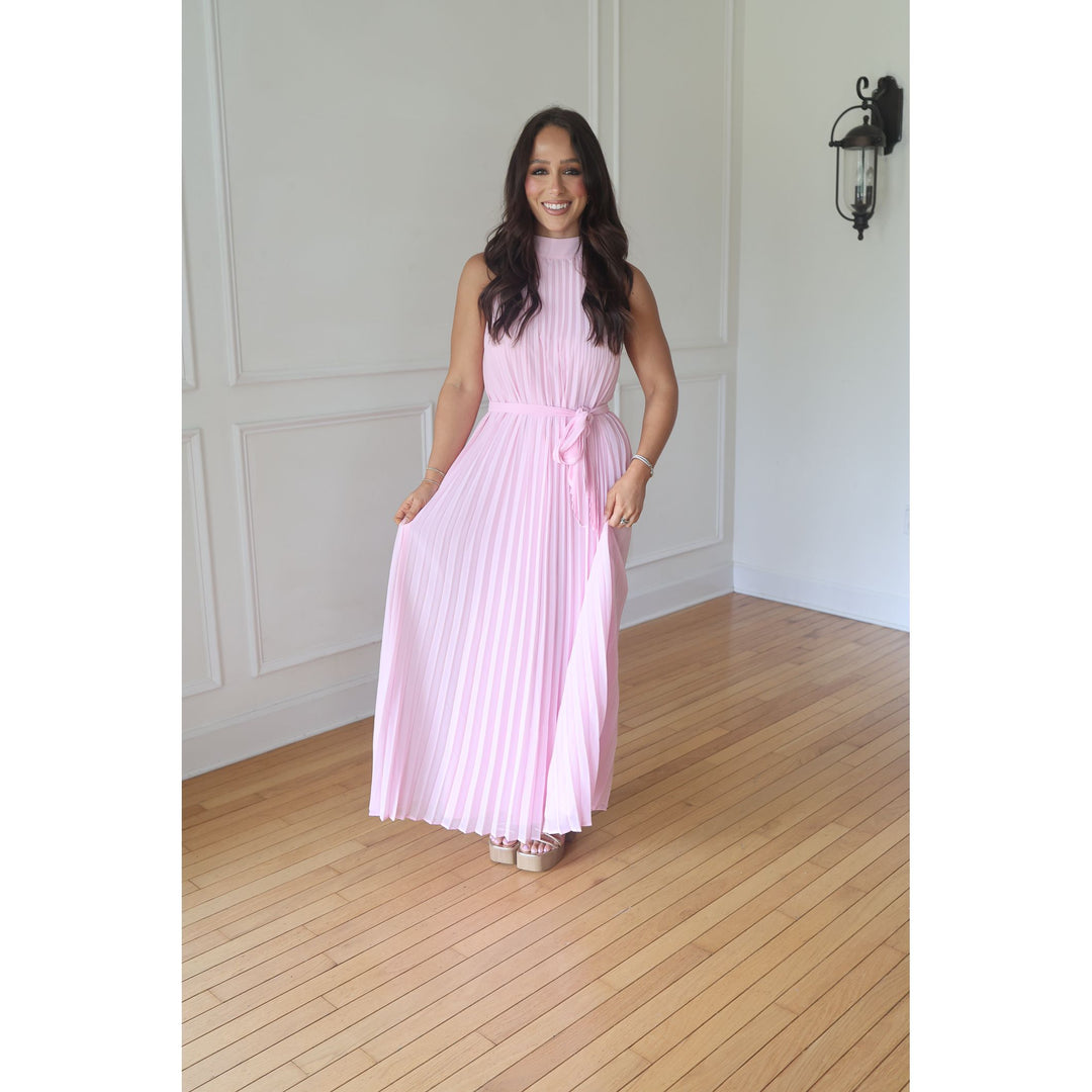 Woman in a pink dress standing in a room with wooden flooring and white walls.