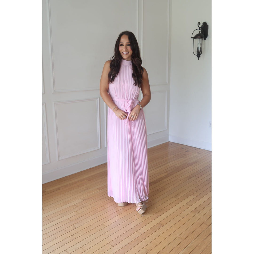 Woman in a pink dress standing in a room with wooden flooring and white walls.