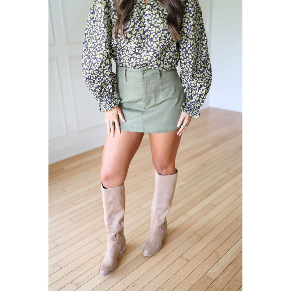 Person wearing a floral blouse, olive skirt, and beige knee-high boots 