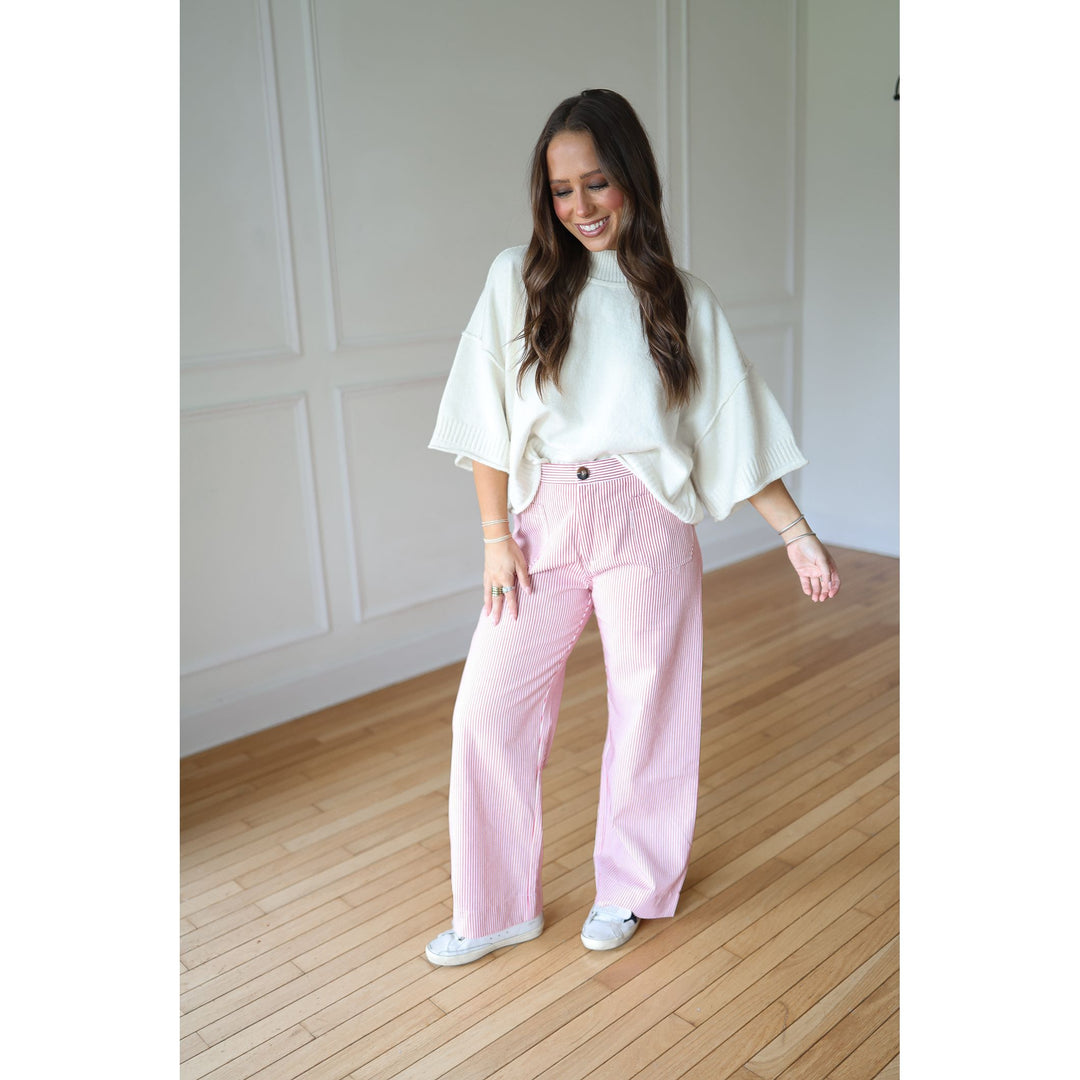 Woman wearing a white top and red striped  pants standing on a wooden floor.