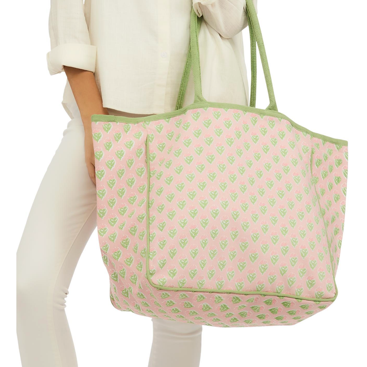 Person holding a pink tote bag with green pattern and handles.