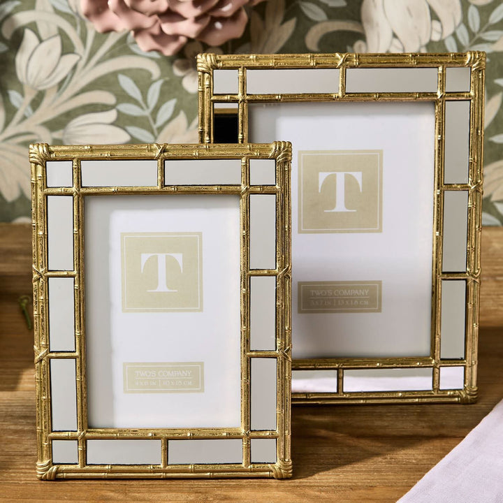 Two gold picture frames with a decorative pattern on a wooden surface.