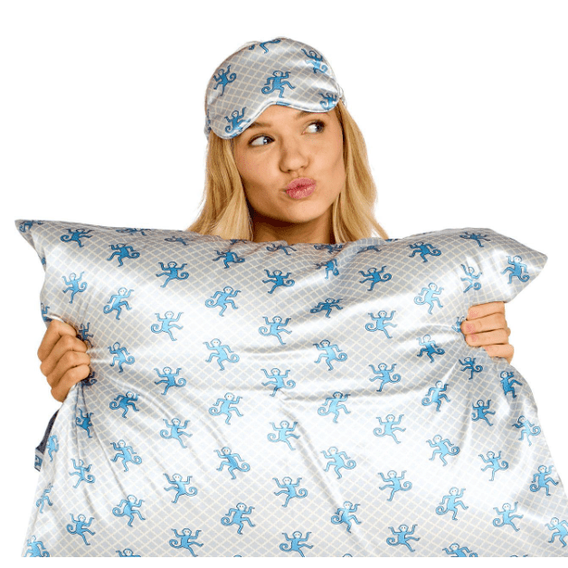 Woman holding a pillow with blue patterns and wearing a matching eye mask.