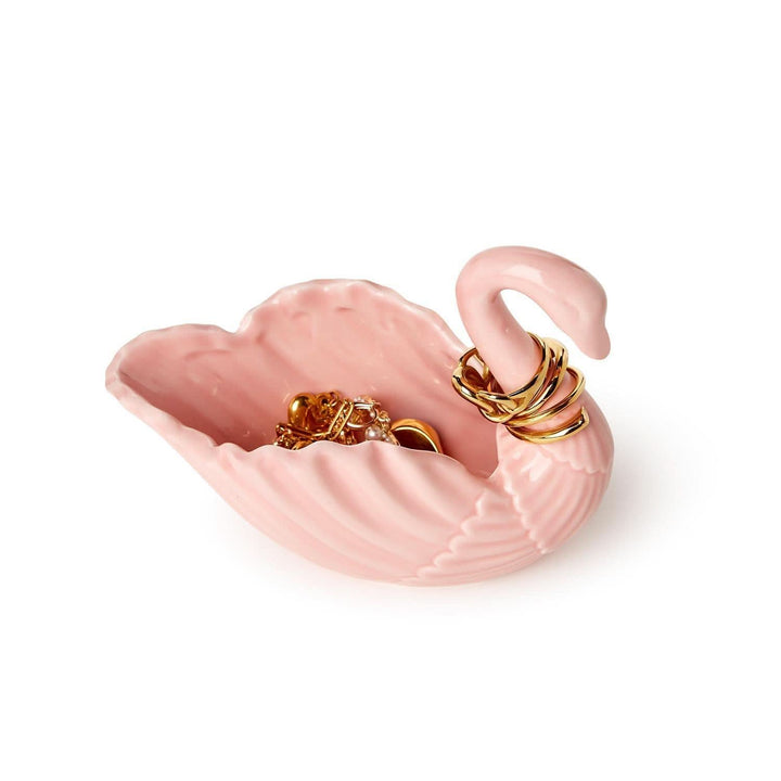 Pink swan-shaped jewelry dish with gold rings on a white background