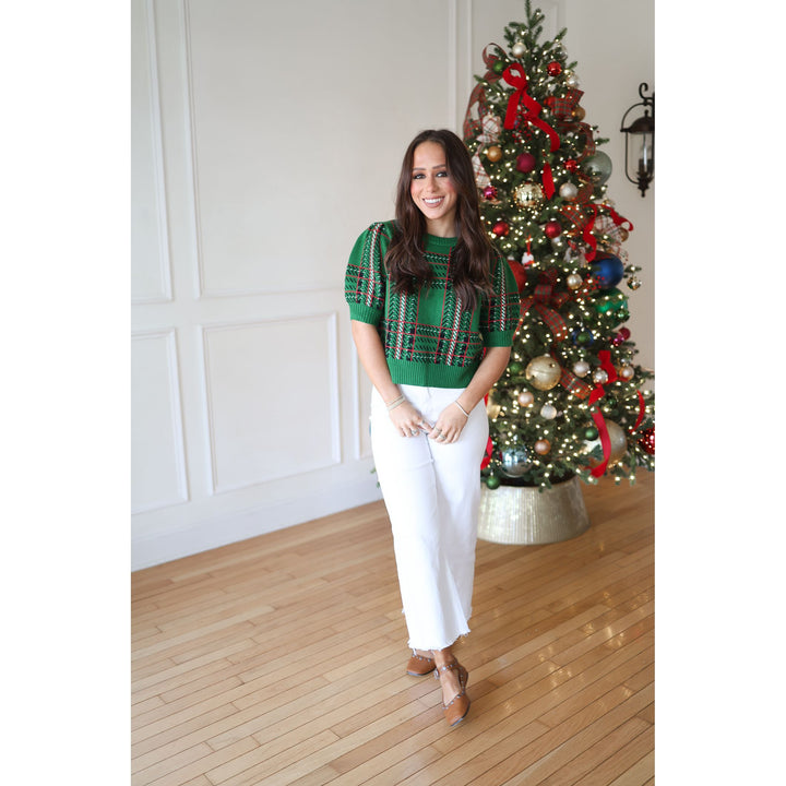 Woman in a green sweater and white pants standing in front of a decorated Christmas tree.