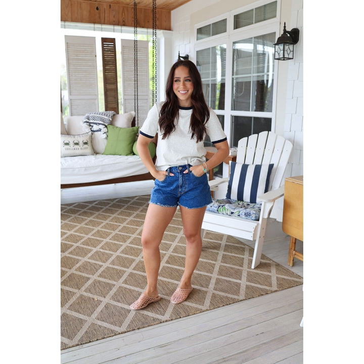 Woman standing on a porch wearing a white t-shirt and blue shorts.