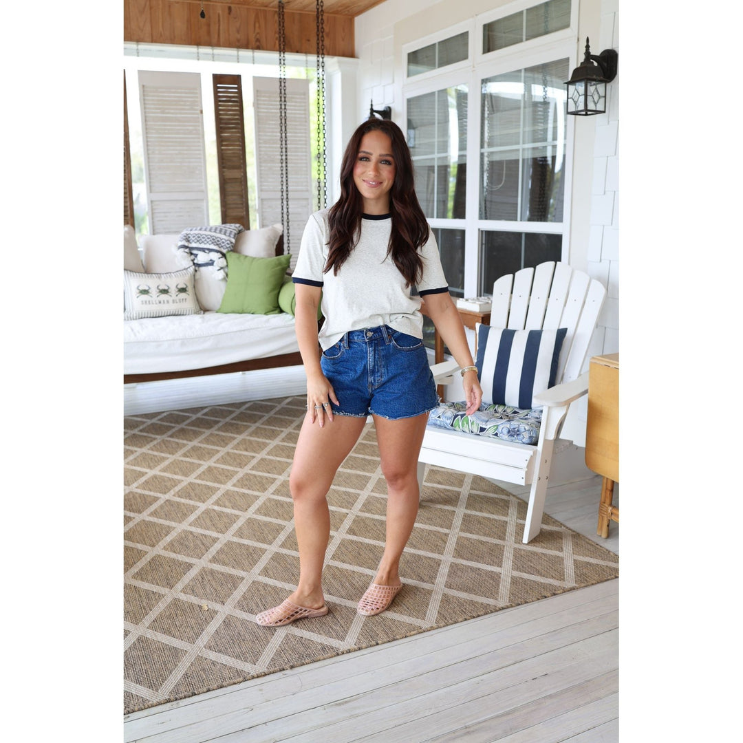 Woman standing on a porch wearing a white t-shirt and blue shorts.