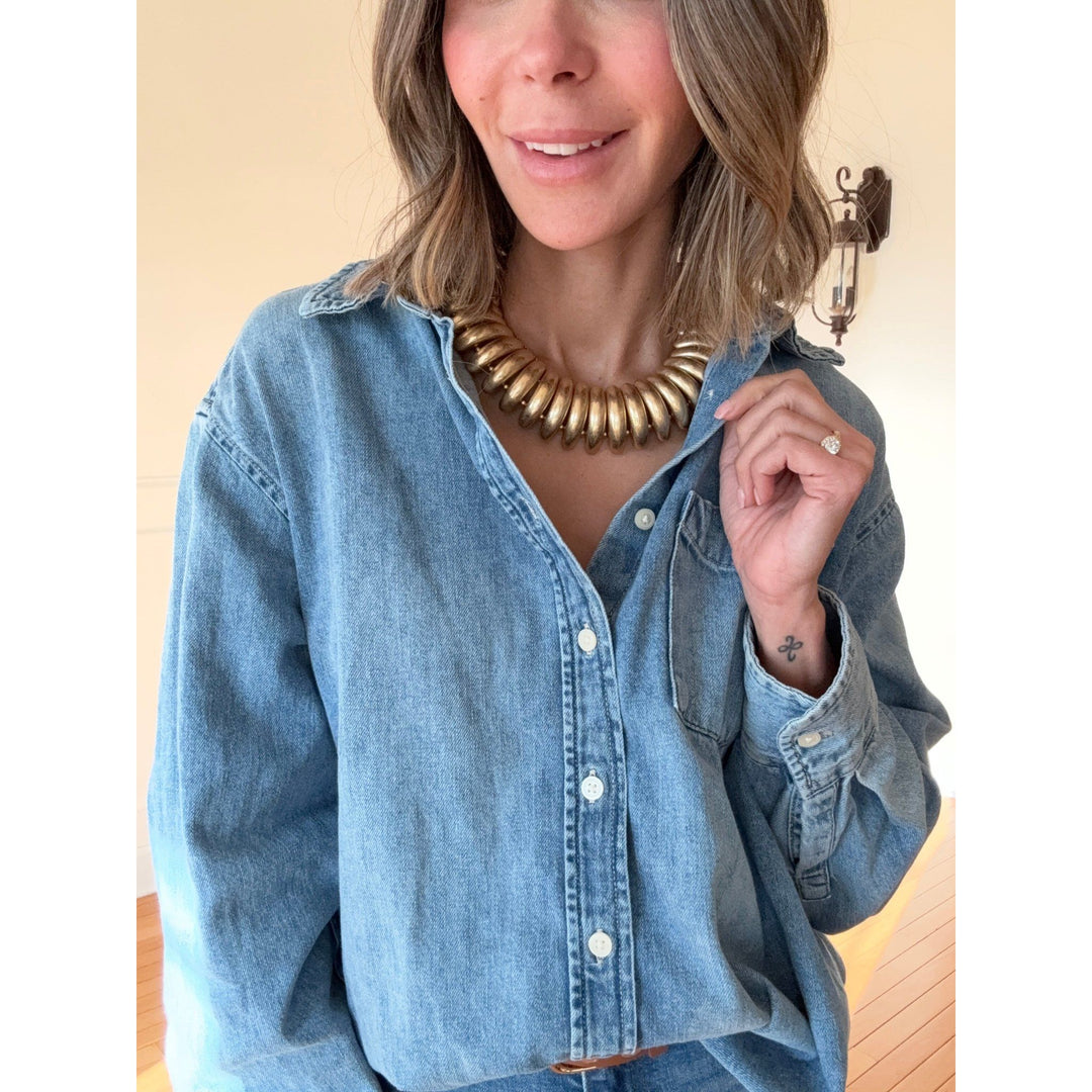 Person wearing a denim shirt with a gold necklace against a neutral background