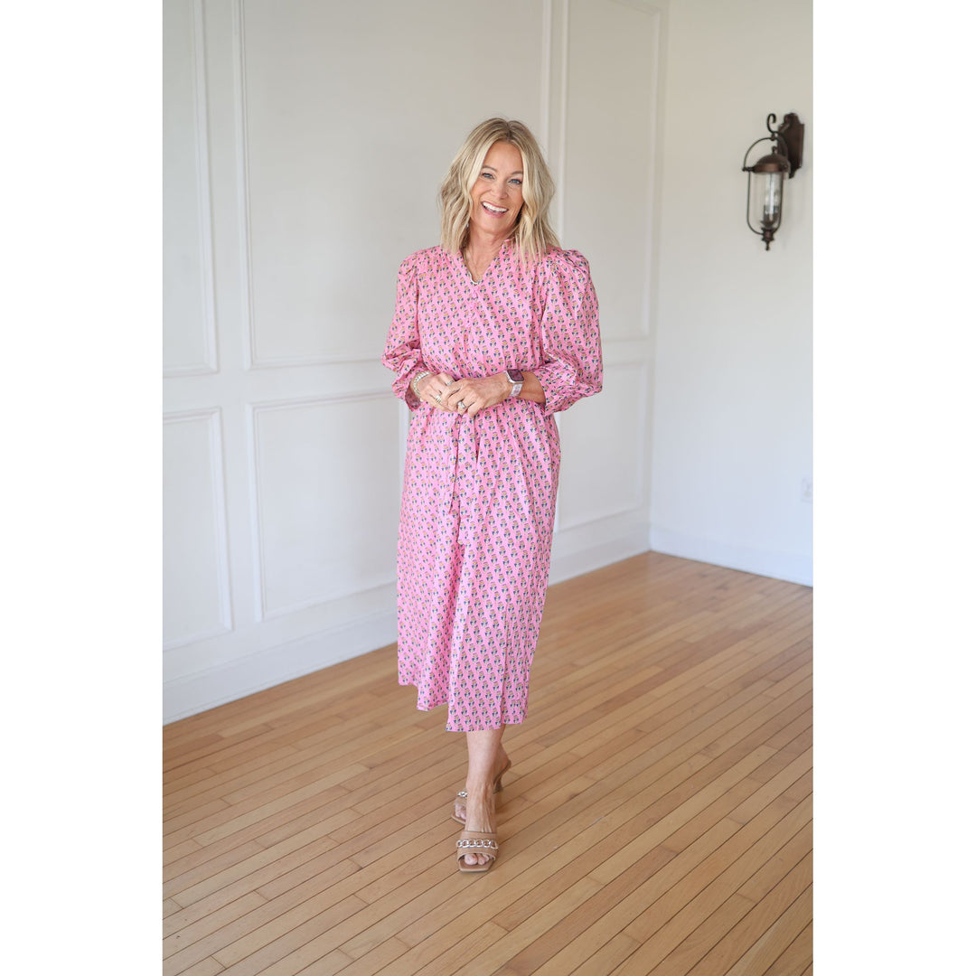 Woman wearing a pink dress with a pattern in a room with wooden flooring and white walls.
