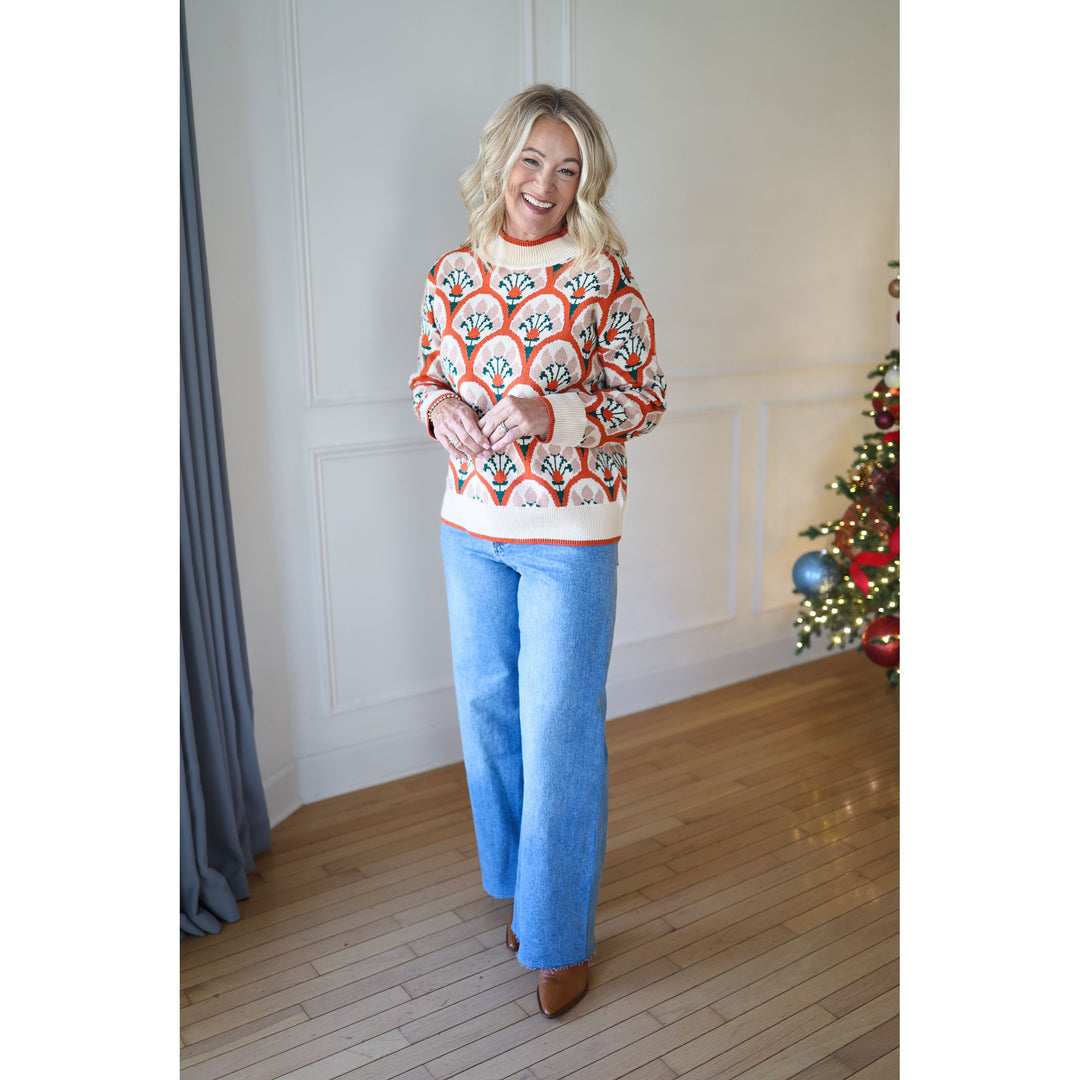 Woman wearing a patterned sweater and blue jeans standing in a room with a Christmas tree.