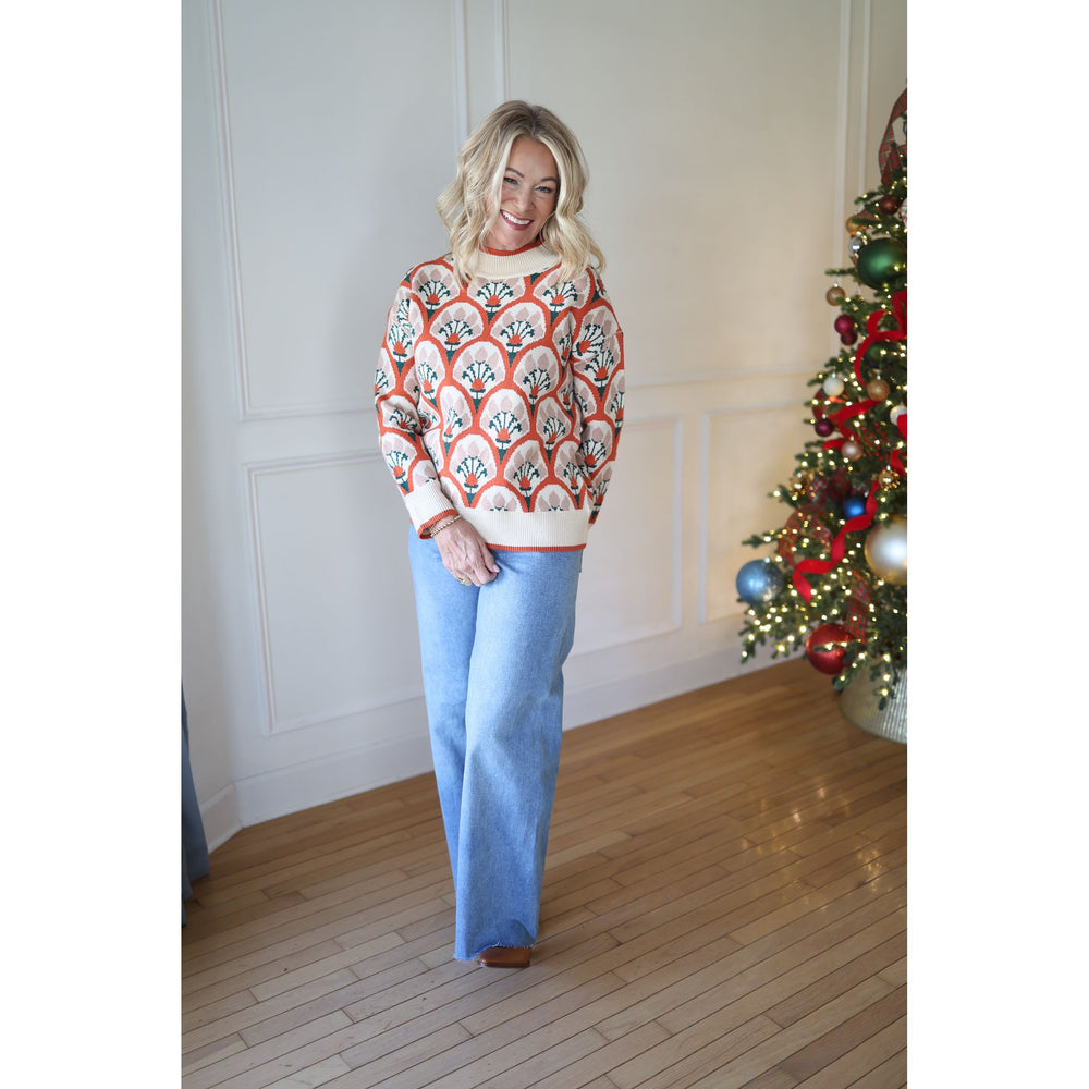 Woman wearing a patterned sweater and blue pants standing in front of a decorated Christmas tree.