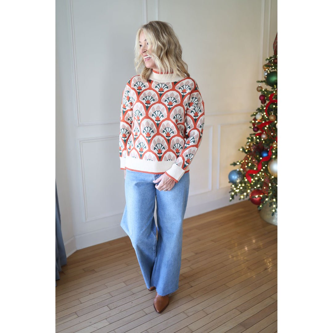 Woman wearing a patterned sweater and blue jeans standing in front of a Christmas tree.