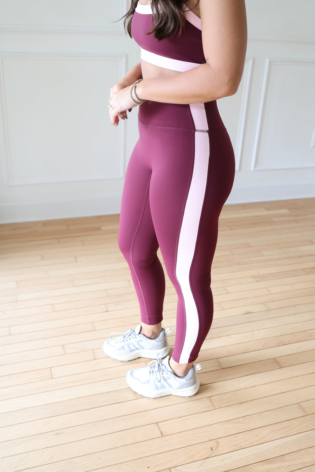 A woman wearing a matching burgundy and light pink activewear set, featuring a sports bra and high-waisted leggings with a vertical pink stripe