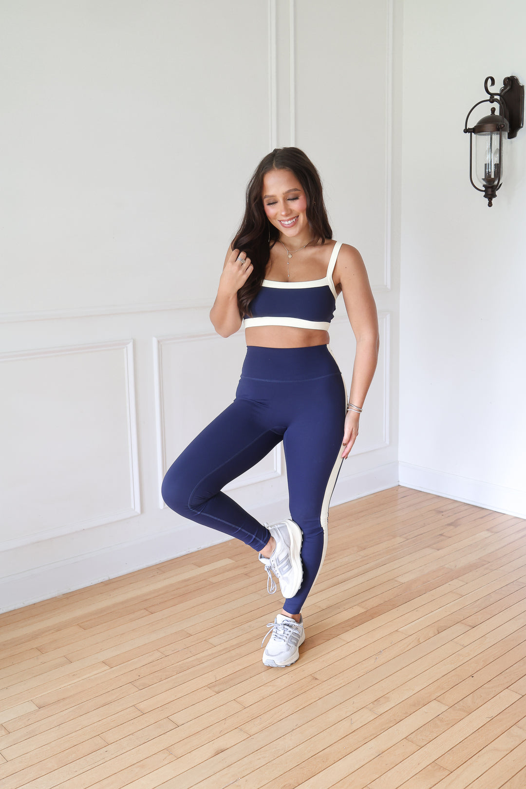 A woman modeling a matching navy blue activewear set consisting of a sports bra and high-waisted leggings with white contrast trim