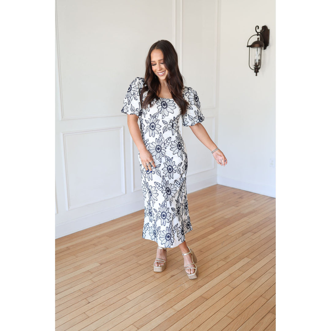 Woman wearing a floral dress standing on a wooden floor with a white wall background