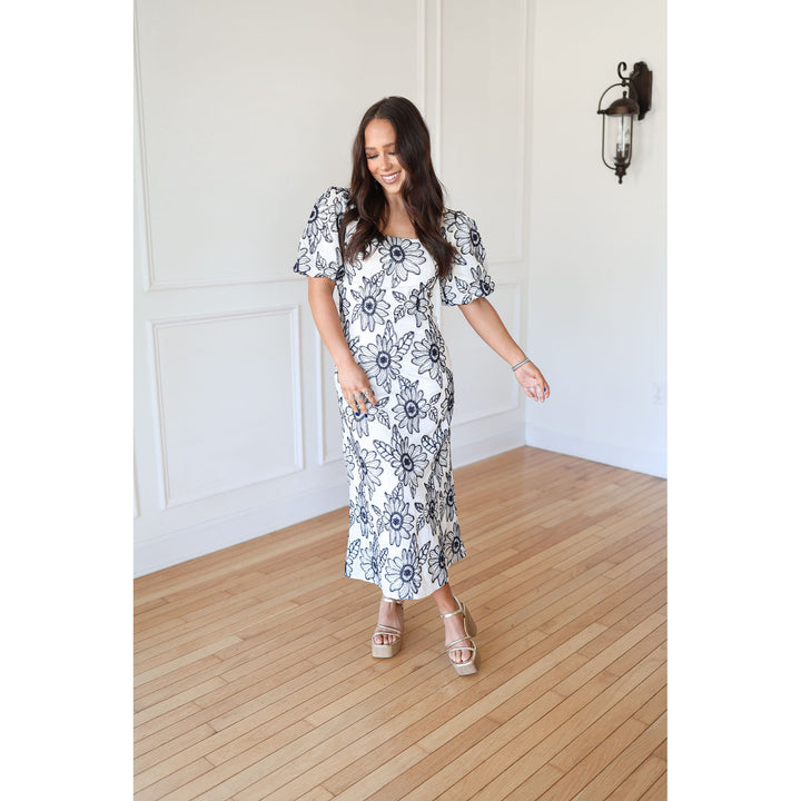 Woman wearing a floral dress standing on a wooden floor with a white wall background