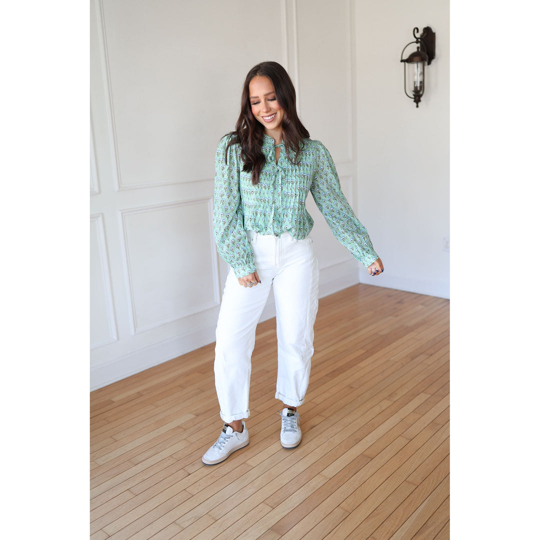 Woman wearing a light green blouse and white pants standing on a wooden floor.