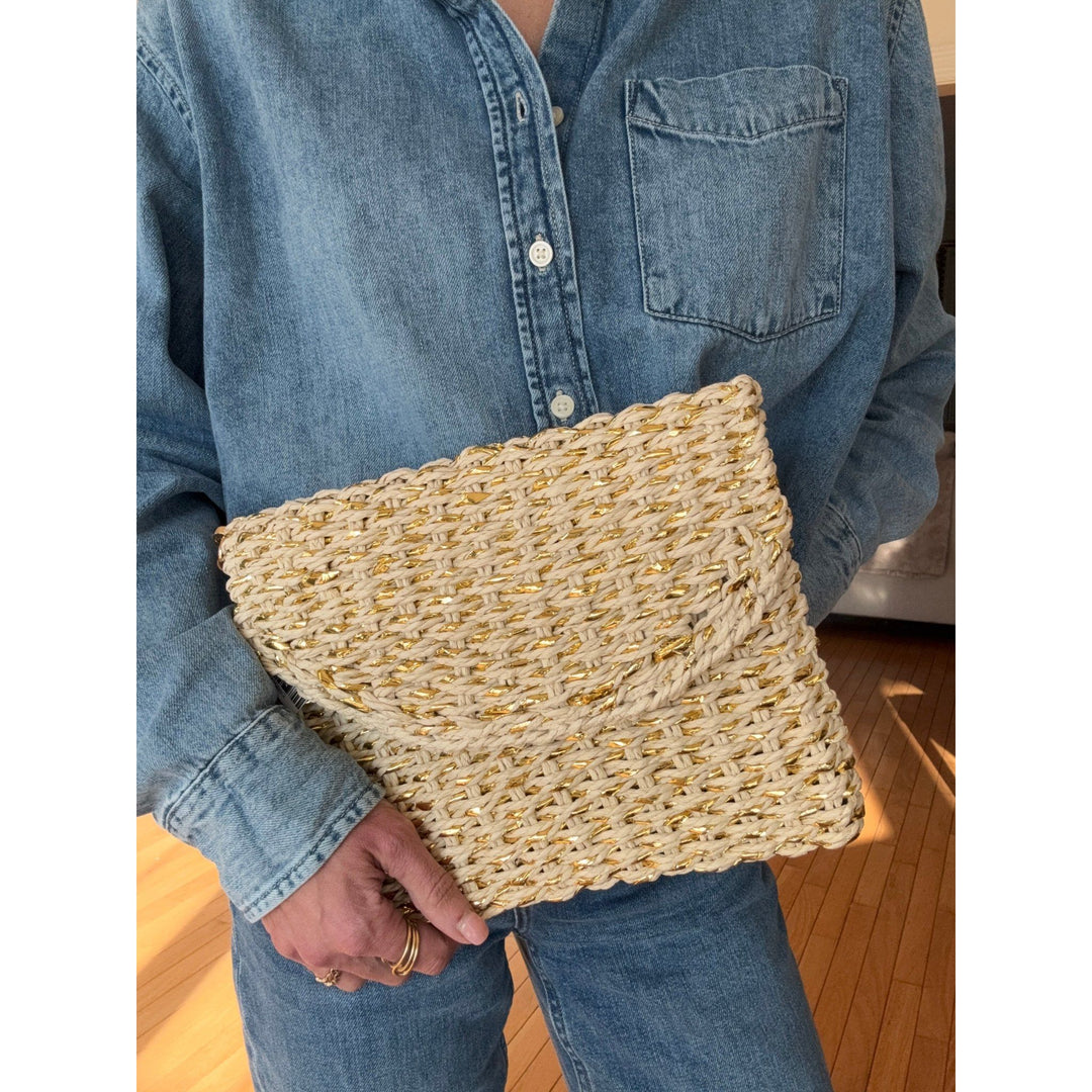 Person holding a woven clutch bag wearing a denim shirt indoors.