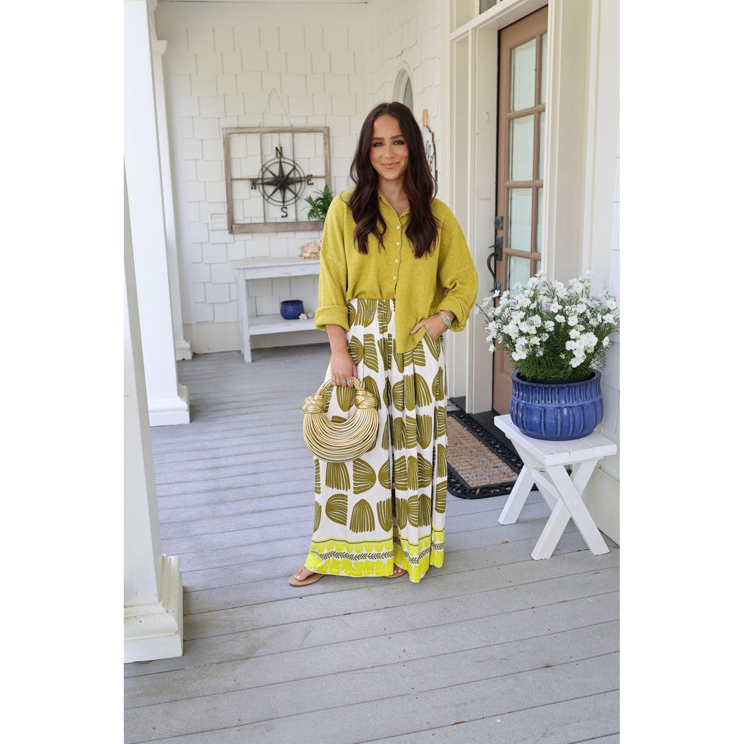 Woman in a yellow top and patterned skirt standing on a wooden porch.