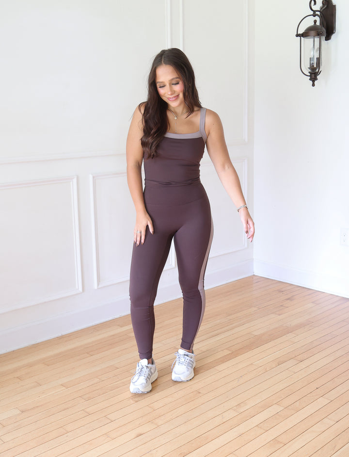 A woman modeling a matching two-piece activewear set consisting of a scoop-neck tank top and high-waisted leggings, in a muted plum-brown color