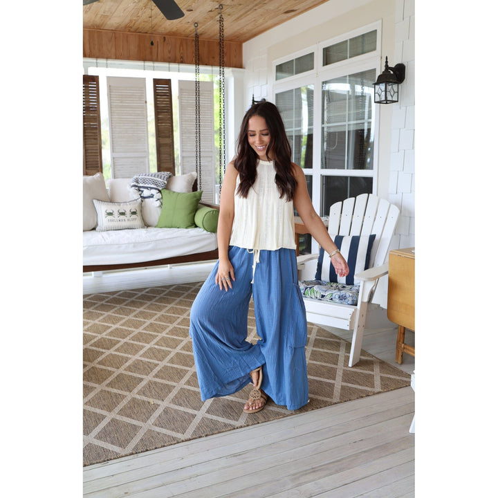 Woman in a white top and blue pants standing on a wooden deck with a house in the background