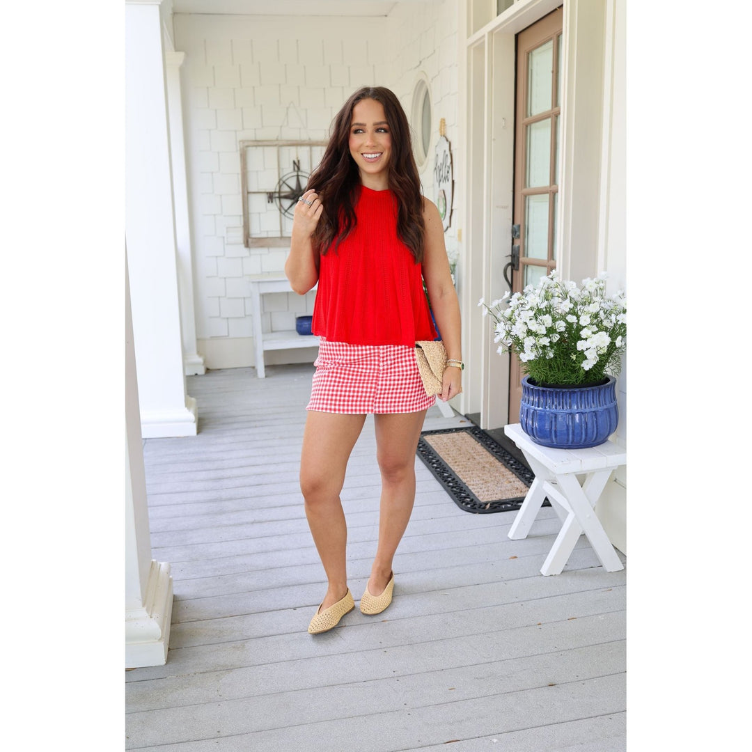 Woman in a red top and checkered skirt standing on a porch.