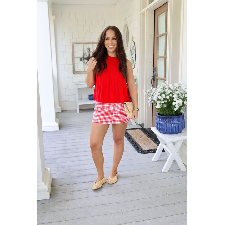 Woman in a red top and checkered skirt standing on a porch.